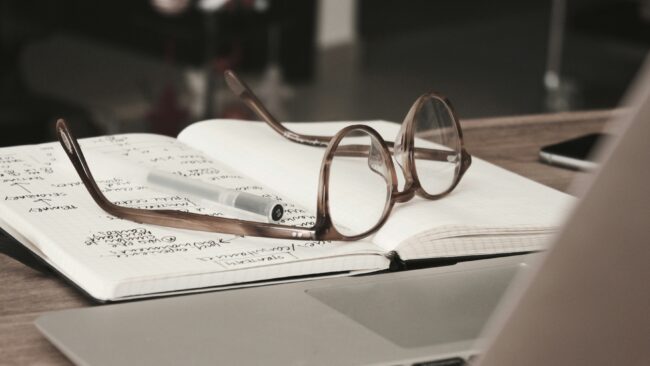 image of a pair of glasses on top of a notebook with a pen